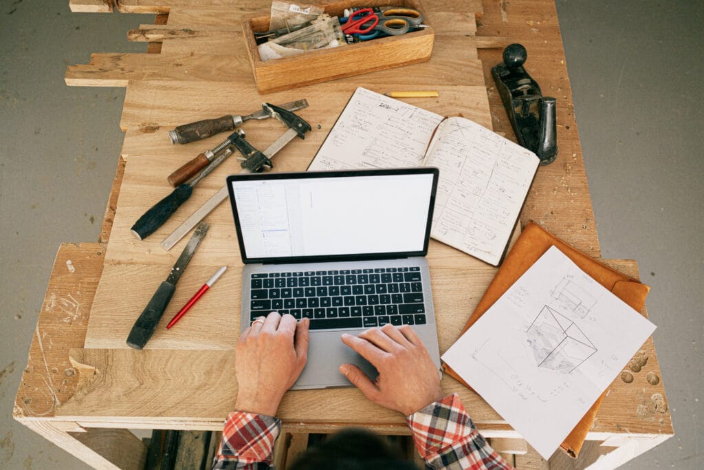A person using a laptop while on the carpentry workbench